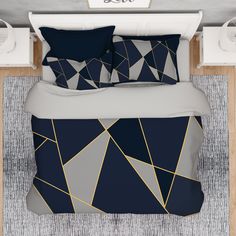 a bed with blue and grey comforters on top of it next to a night stand