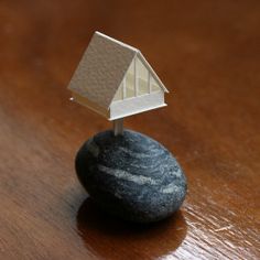 a small house sitting on top of a black rock next to a wooden table with a brown floor