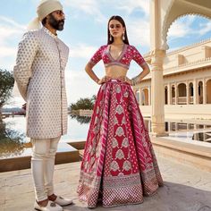 a man standing next to a woman in a red and white lehenga suit