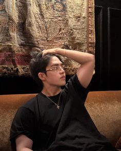 a young man sitting on top of a couch next to a wall hanging with paintings