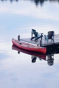 a red boat sitting on top of a lake next to a dock with two chairs