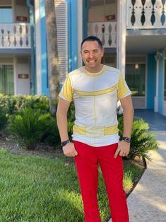 a man standing in front of a building wearing red pants and a white shirt with yellow trim