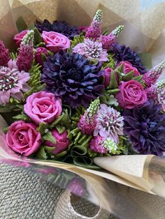 a bouquet of purple and pink flowers sitting on top of a piece of paper next to a burlap bag