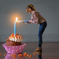 a woman lighting a candle on top of a cupcake with frosting and sprinkles