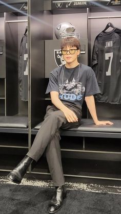 a young man sitting on top of a bench in front of a locker room filled with jerseys