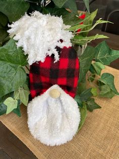 a stuffed santa clause is sitting on a table next to some ivy and other greenery