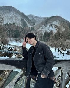 a young man standing on top of a snow covered slope next to a wooden fence