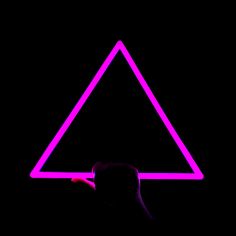 a person holding up a neon pink triangle in front of a black background with an orange light