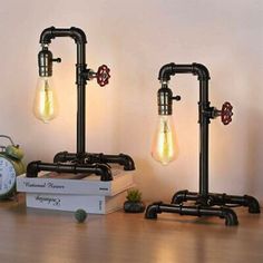 two industrial style lamps are sitting on a table next to books and an alarm clock