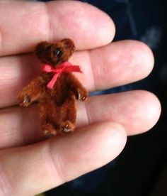 a small teddy bear is held in someone's hand with a red ribbon on it