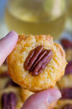 a hand holding up a cookie with a pecan on it's center and some nuts in the background