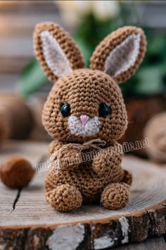 a small crocheted bunny sitting on top of a wooden stump with its eyes open