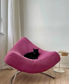 a black cat is sitting in a pink chair