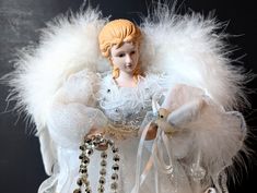 an angel doll holding a teddy bear with white feathers and beads on it's chest