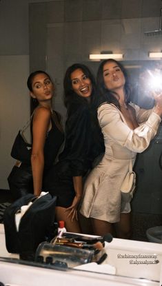 three beautiful women taking a selfie in front of a mirror with their cell phone