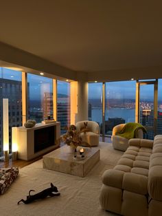 a living room filled with furniture and large windows overlooking the city at night or dawn