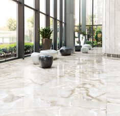 an indoor area with large windows and white marble flooring, potted plants on either side