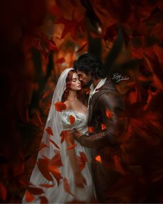 a bride and groom standing in front of red leaves with their arms around each other