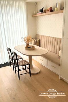 a dining table with four chairs and a bench in front of a window that has white curtains