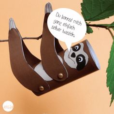 a paper sloth hanging from a tree branch with a speech bubble above it