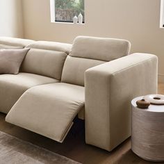 a beige couch with pillows on it in a living room next to a round table