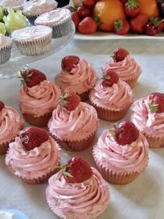 several cupcakes with pink frosting and strawberries on the top are arranged in rows