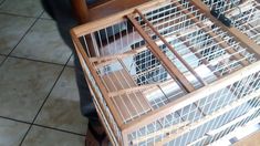 a small bird cage sitting on top of a wooden table next to a person's leg