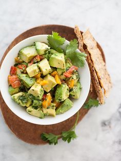 a white bowl filled with avocado, tomatoes and cilantro on top of a wooden cutting board