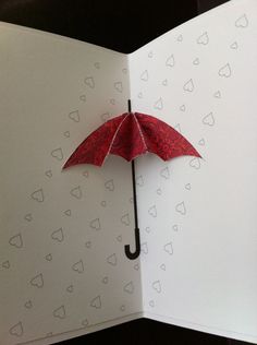 an open book with a red umbrella sticking out of it's cover and hearts drawn on the pages