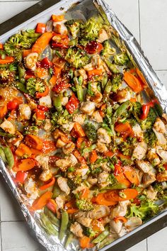 a pan filled with chicken, broccoli and carrots covered in tin foil