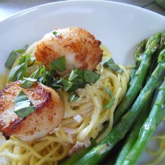 scallops, asparagus and pasta on a white plate with green garnish