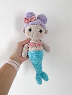 a crocheted mermaid doll being held by a person's hand on a white background