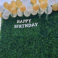 balloons are floating in the air above a green wall with happy birthday written on it