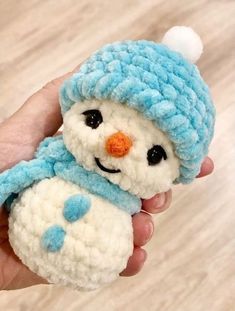 a hand holding a small crocheted snowman with a blue hat and scarf