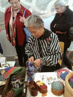 an older woman is working on crafts at a table with other people in the background