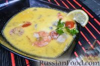 a black bowl filled with soup and garnished with shrimp, lime and tomatoes