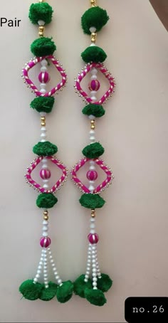 a pair of green and pink beaded earrings with pom - poms hanging from it