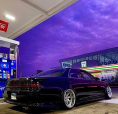 a black car is parked in front of a gas station at night with purple clouds