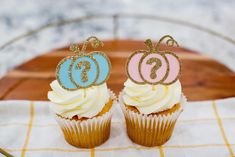 two cupcakes with frosting and glitter decorations on them sitting on a table