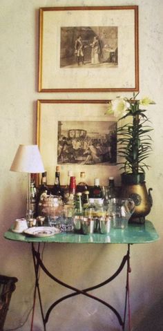 a green table topped with lots of bottles and glasses next to a painting on the wall