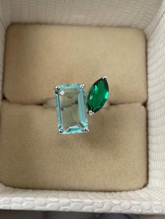 an emerald and diamond ring sitting on top of a cushioned white box in a display case