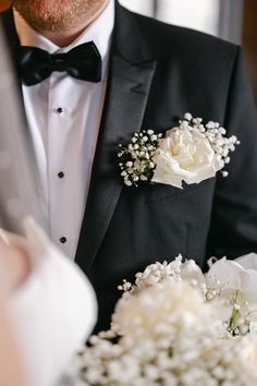 a man in a tuxedo with white flowers on his lapel and black bow tie