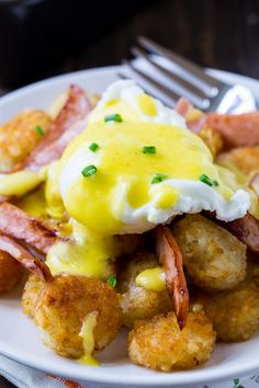 a white plate topped with fried potatoes covered in gravy and bacon next to a fork