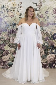 a woman wearing a white dress standing in front of a wall with flowers on it