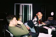 two men sitting at a desk in front of a computer monitor and sound mixing equipment