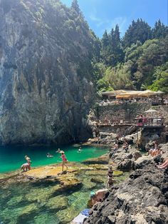 people are swimming in the clear blue water next to some cliffs and trees, while onlookers watch