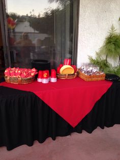 the table is set up outside with red and black cloth on it, along with two baskets full of food