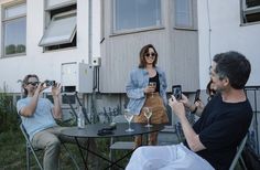 three people sitting at a table with wine glasses in front of them, taking pictures