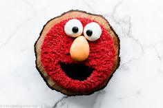 a red cake with eyes and nose on top of a white marble countertop next to a piece of wood