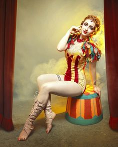 a woman dressed as a clown sitting on top of a barrel